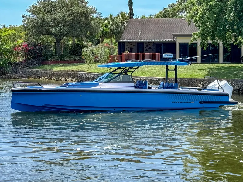 The Image of 2025 Axopar 37 Sun Top BRABUS Trim boat on calm water near a house. - 0