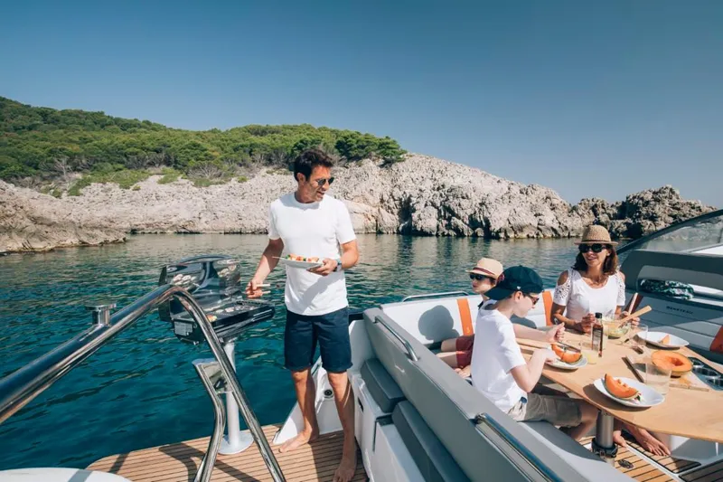 Slide: The Image of Family enjoying a meal on a 2024 Beneteau Flyer 10 boat in a scenic bay. - 32