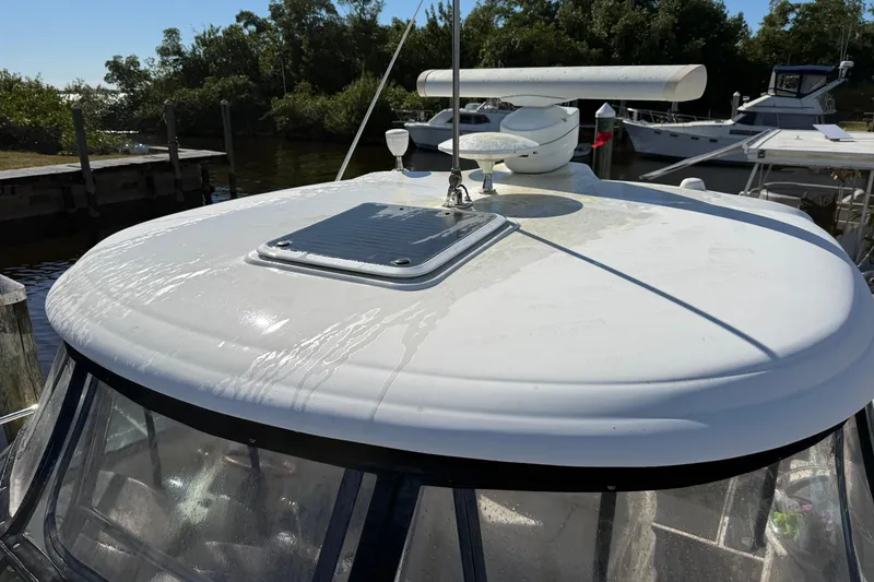 Slide: The Image of 2005 Sea Ray 390 Sundancer boat roof with radar and hatch, docked near trees. - 12