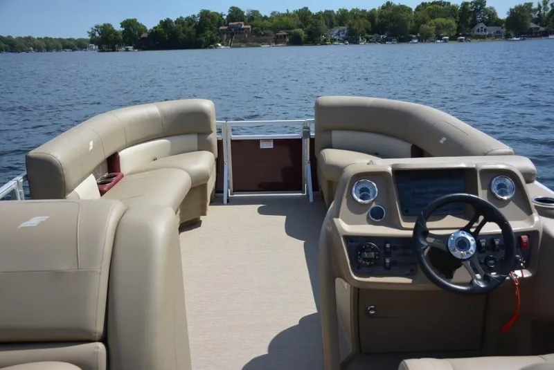 Slide: The Image of 2024 Starcraft 20 LX pontoon boat interior with beige seating and steering console on a lake. - 12