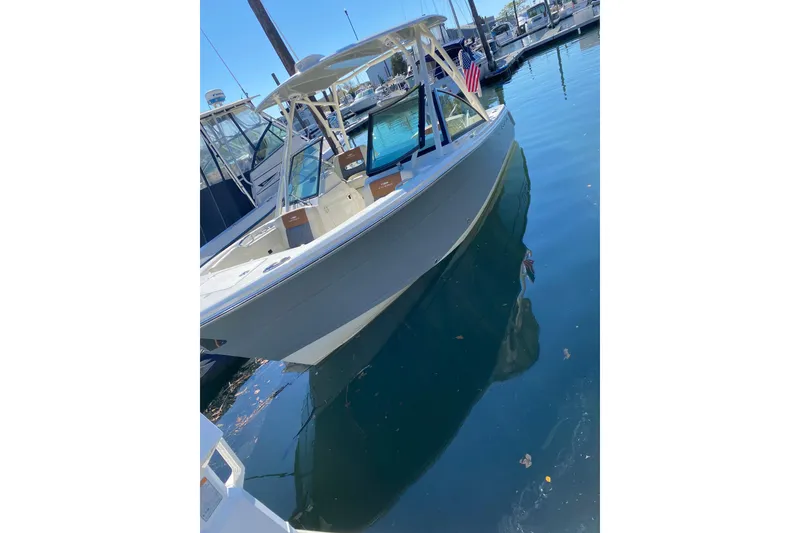 Slide: The Image of 2022 Cobia 240 Dual Console boat docked in marina, reflecting on water. - 6