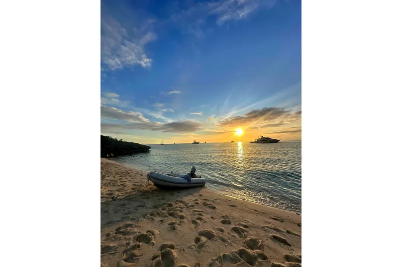 Slide: The Image of Sunset over ocean with boats, sandy beach, and inflatable dinghy in foreground. - 45