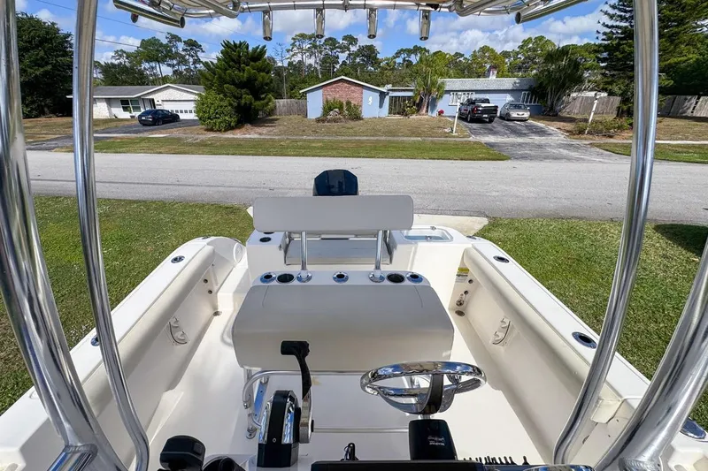 Slide: The Image of 2022 Cobia 220 Center Console boat interior with steering wheel and seating, parked in a residential area. - 64