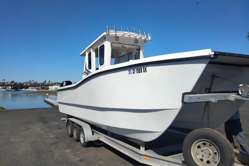 Slide: The Image of 2021 Custom Pilot House Catamaran on trailer by waterfront under clear blue sky. - 14