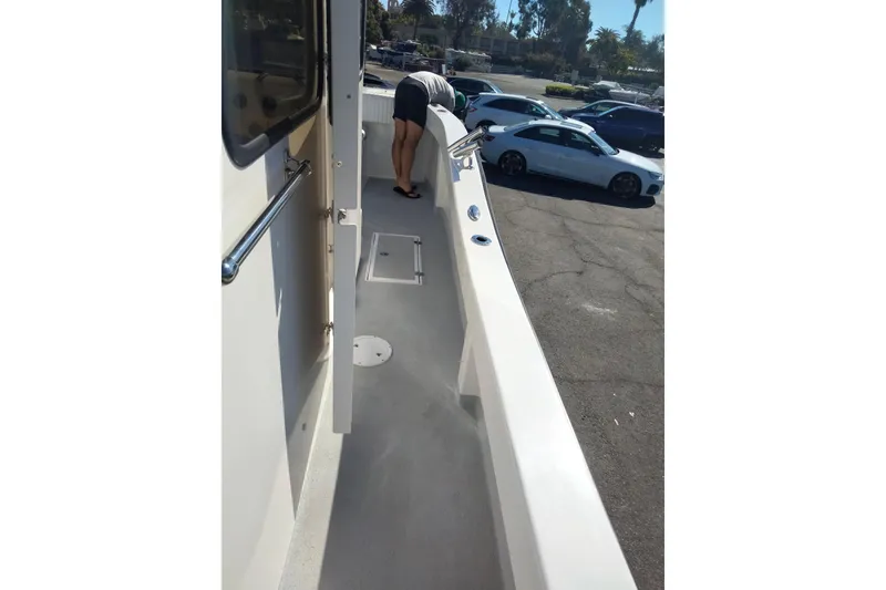 Slide: The Image of 2021 Custom Pilot House Catamaran deck with person inspecting, parked cars in background. - 19