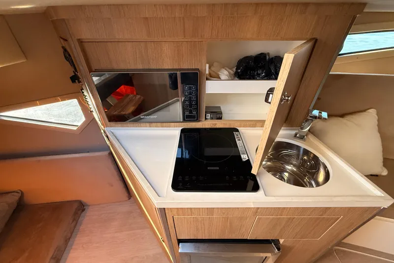 Slide: The Image of Compact kitchen area in 2023 NX Boats 360 Sport Coupe with sink, stove, and microwave. - 29