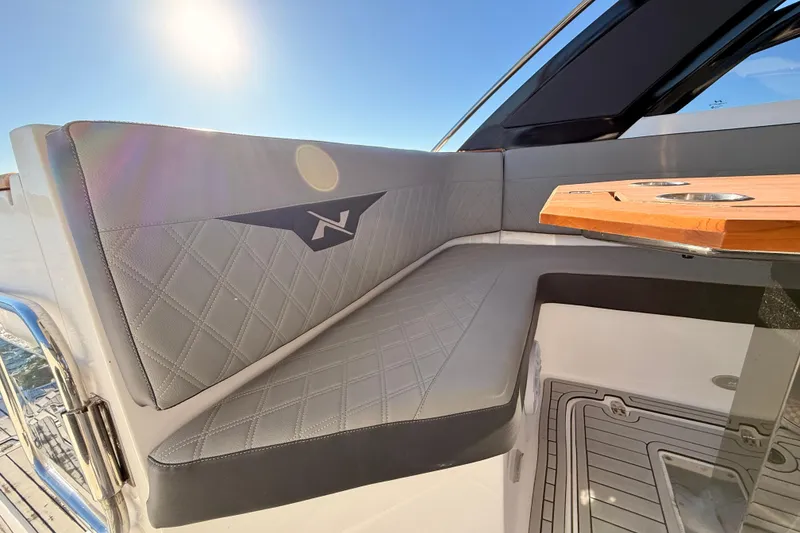 Slide: The Image of 2023 NX Boats 360 Sport Coupe interior with luxurious seating and wooden table under sunlight. - 40