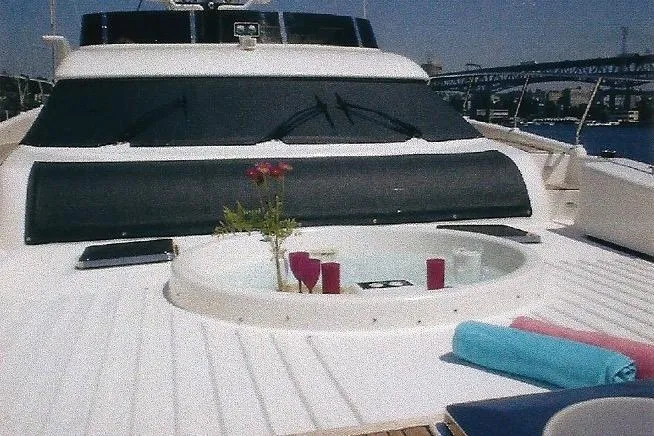 Slide: The Image of Luxury Dyna Laguna yacht deck with hot tub, flowers, and towels, set against a scenic bridge backdrop. - 21