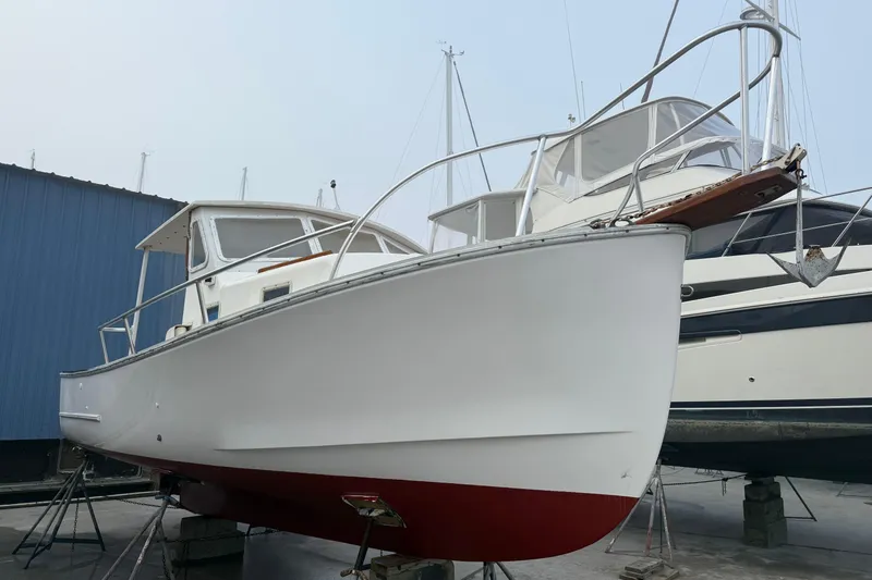 Slide: The Image of 1983 SISU 26 boat on dry dock, white hull with red bottom, near blue building. - 8