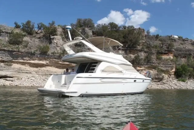 The Image of 1999 Maxum 4600 SCB yacht on calm water near rocky shoreline. - 0