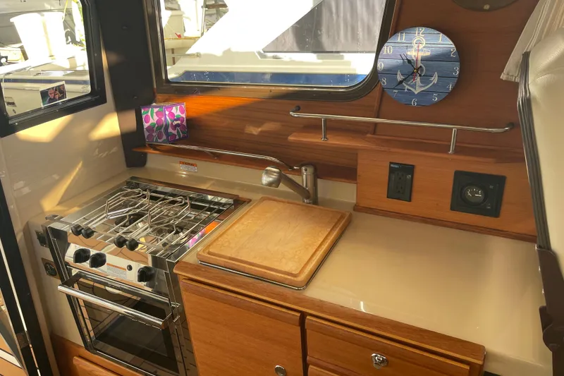 Slide: The Image of 2019 Ranger Tugs R-27 interior kitchen with stove, cutting board, and nautical clock. - 2