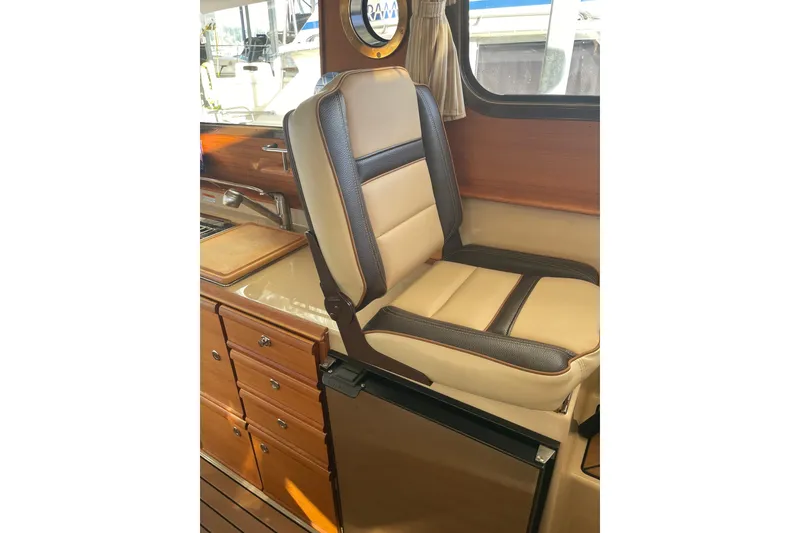 Slide: The Image of 2019 Ranger Tugs R-27 interior with beige and brown seating, wooden cabinetry, and window view. - 29