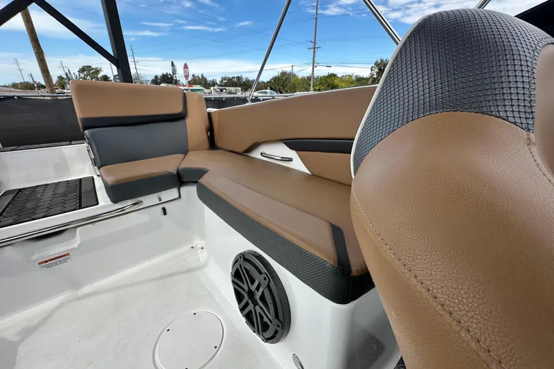 Slide: The Image of 2023 Scarab 215 ID boat interior with brown and black seating, speaker, and blue sky background. - 56