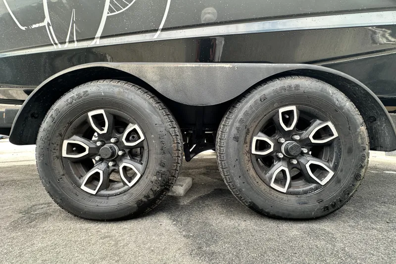 Slide: The Image of 2023 Scarab 215 ID trailer wheels, black with silver accents, parked on asphalt. - 72