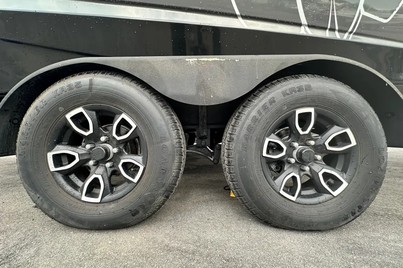 Slide: The Image of 2023 Scarab 215 ID trailer wheels with black and silver rims on pavement. - 73