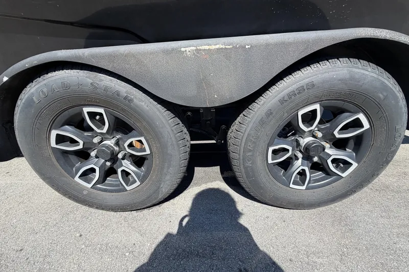 Slide: The Image of 2023 Scarab 215 ID trailer wheels, Load Star tires, black alloy rims, outdoor setting. - 74