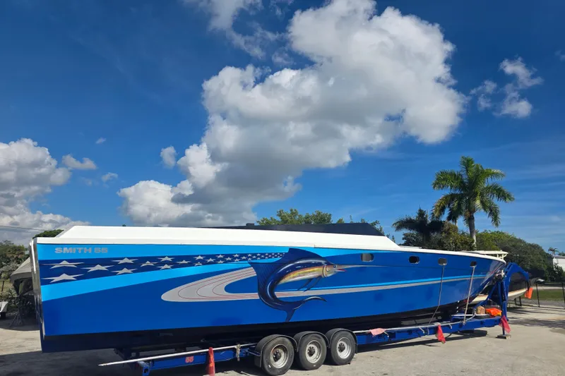 Slide: The Image of 2025 Don Smith Custom 55' boat with vibrant blue design on trailer under clear sky. - 2