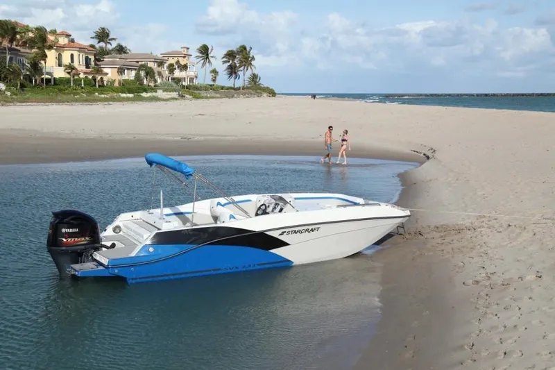 Slide: The Image of 2024 Starcraft 231 SVX boat beached on a sandy shore with people in the background. - 2