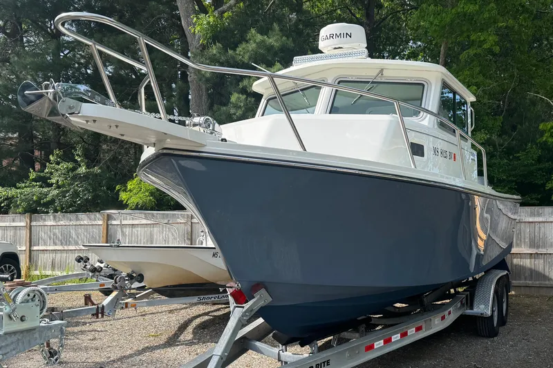 The Image of 2023 Parker 2520 XLD Sport Cabin boat on trailer, surrounded by trees and fencing. - 0