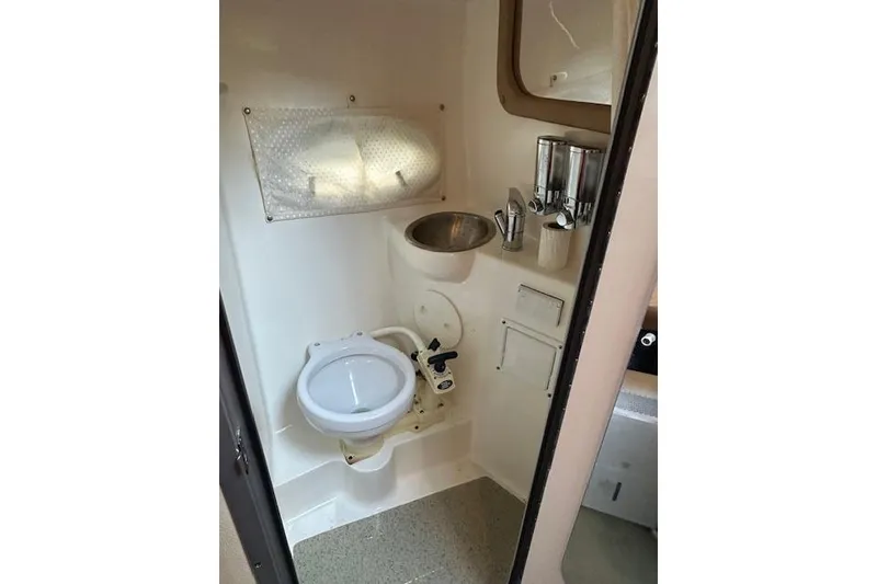 Slide: The Image of 2014 Rinker 260 Express Cruiser bathroom with toilet, sink, and dispensers. - 17