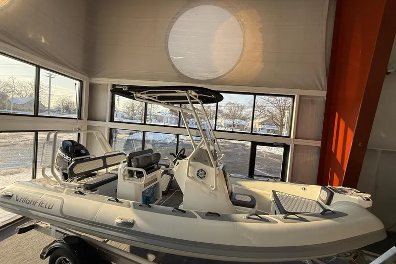 Slide: The Image of 2026 Highfield Sport 560 boat displayed indoors with Suzuki engine. - 2