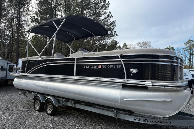 Slide: The Image of 2020 Harris Cruiser 250 pontoon boat on trailer, parked in wooded area. - 24