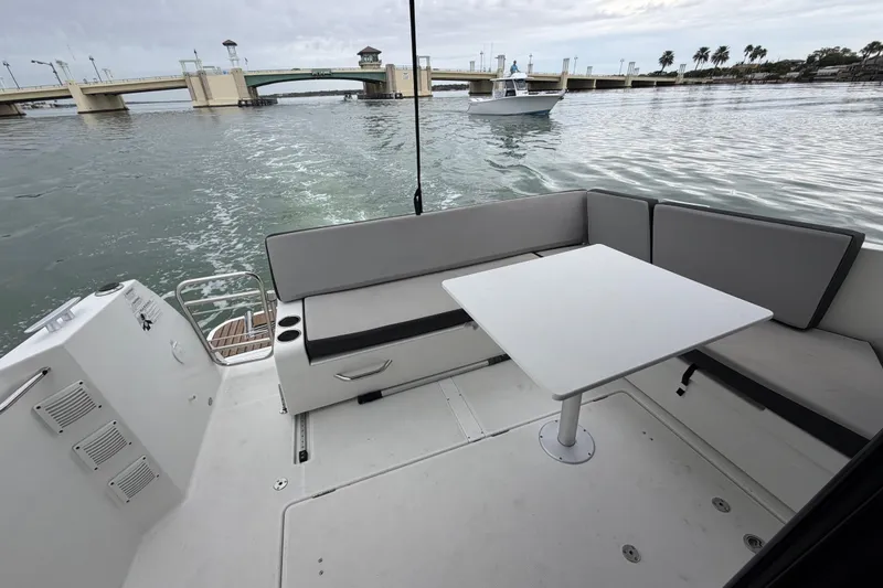 Slide: The Image of 2019 Jeanneau NC 895 boat deck with seating and table, near a bridge on calm water. - 9