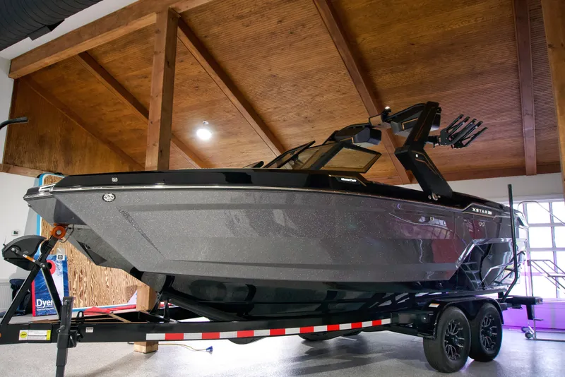 The Image of 2025 MasterCraft XStar 23 boat on trailer in showroom with wooden ceiling. - 1
