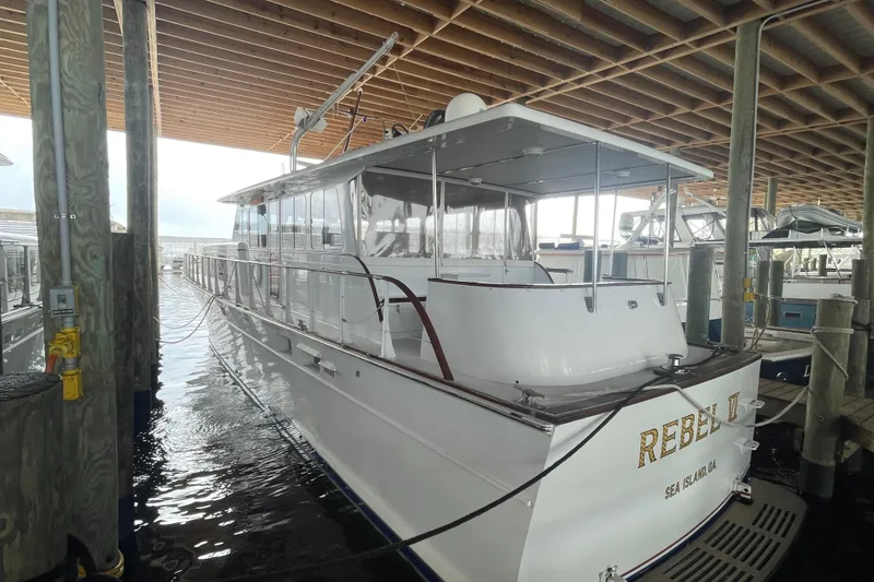 Slide: The Image of 1967 Huckins Offshore yacht docked in a marina, named "Rebel II," under a wooden canopy. - 6