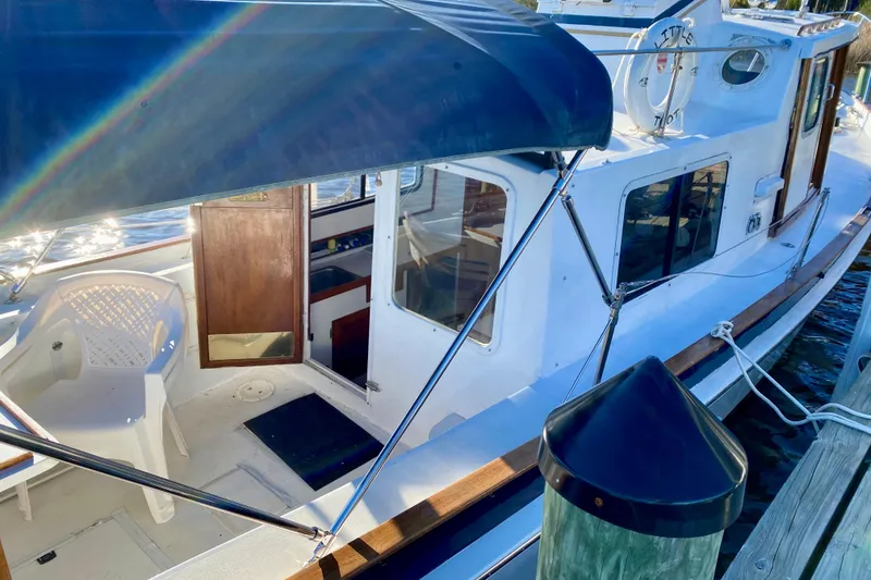 Slide: The Image of 1979 Outer Reef 26/31 boat docked, featuring a canopy and open cabin door. - 8