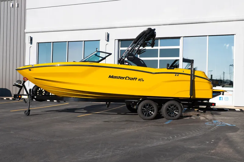 Slide: The Image of 2026 MasterCraft NXT23 boat in vibrant yellow on a trailer outside a building. - 2