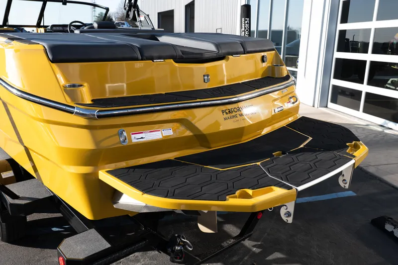 Slide: The Image of 2026 MasterCraft NXT23 boat, yellow exterior, rear view with swim platform, parked outdoors. - 5
