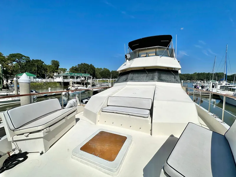 Slide: The Image of 1987 Hatteras 54 Motoryacht docked, featuring spacious deck seating under clear blue skies. - 34