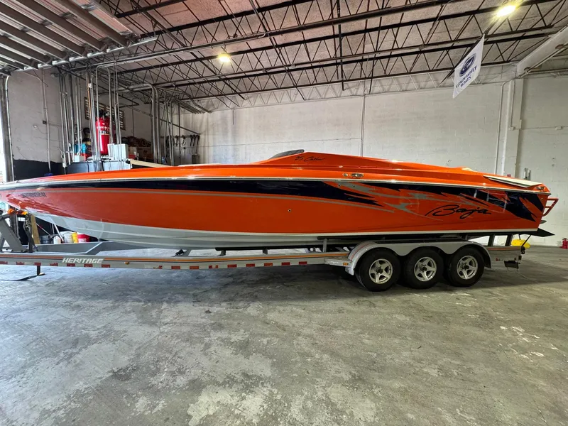 The Image of 2007 Baja 35 Outlaw speedboat in vibrant orange, parked on a trailer in a warehouse. - 1