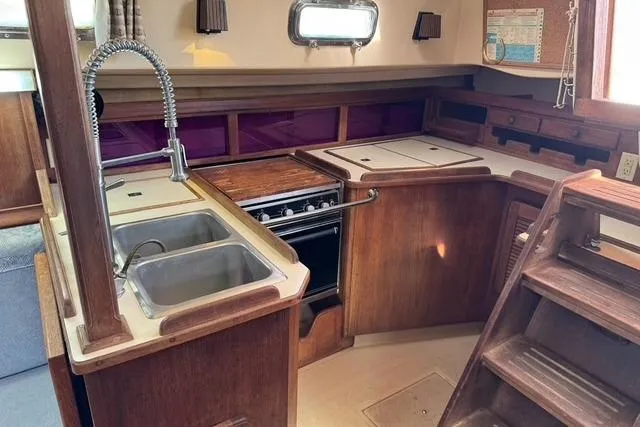 Slide: The Image of 1989 Island Packet 35 yacht kitchen with dual sinks, stove, and wooden cabinetry. - 28