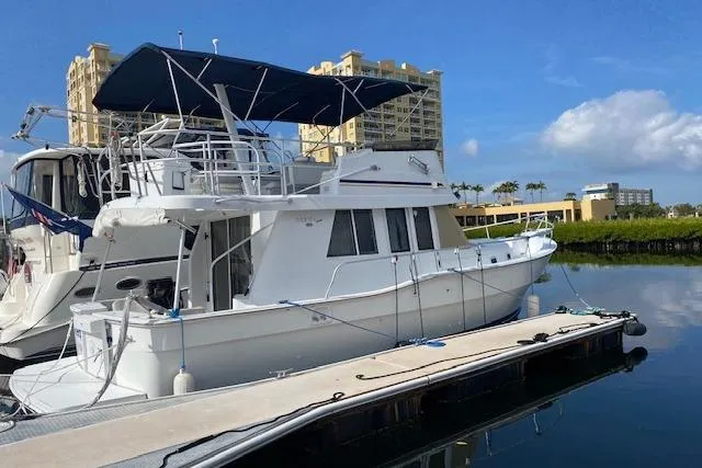 The Image of 1999 Mainship 350 Trawler docked at marina, blue canopy, clear sky background. - 0