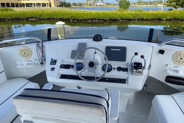 Slide: The Image of 1999 Mainship 350 Trawler helm with steering wheel, controls, and Raymarine display by waterfront. - 11