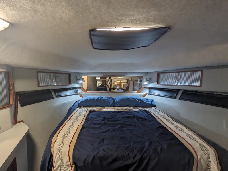 Slide: The Image of 1988 Sea Ray 390 Express Cruiser cabin with bed, blue bedding, and overhead hatch. - 31