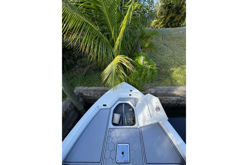Slide: The Image of Bow of 2022 Avid 23 FS Magnum boat with open storage compartment, near lush greenery. - 14