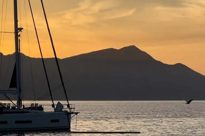 Slide: The Image of Sailboat Amel 50 at sunset with mountain silhouette and whale tail in the distance. - 67