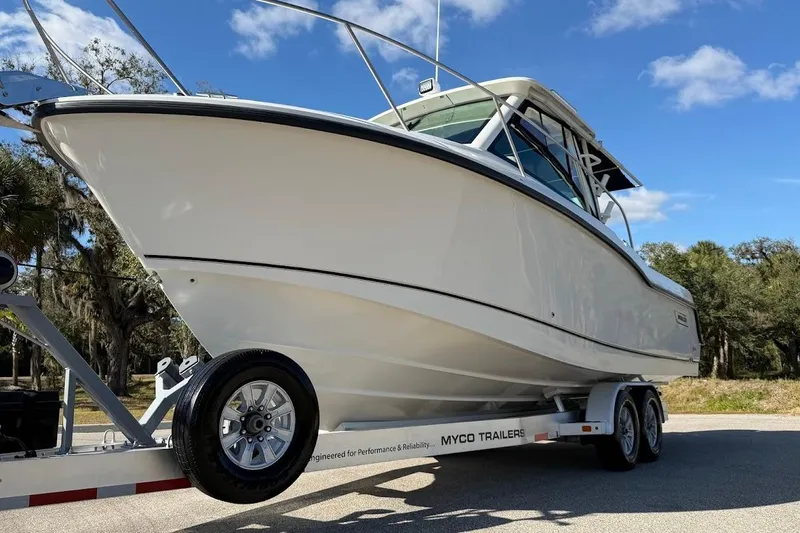 Slide: The Image of 2017 Boston Whaler 285 Conquest boat on trailer, parked outdoors under blue sky. - 17