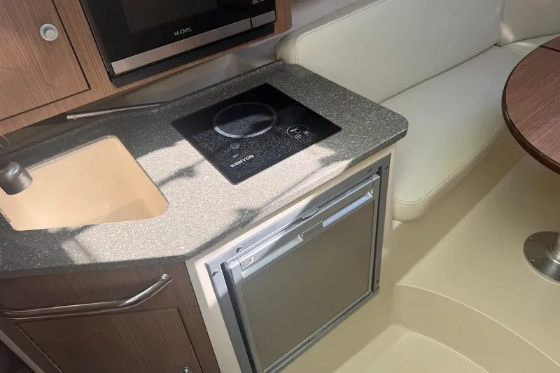 Slide: The Image of 2017 Boston Whaler 285 Conquest interior with kitchenette, featuring sink, stove, and seating area. - 35
