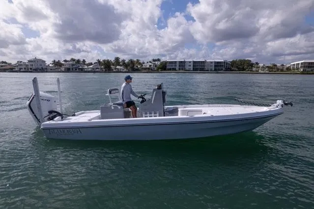 Slide: The Image of 2024 Islamorada Boatworks 24 on water, person steering, cloudy sky, waterfront buildings in background. - 57