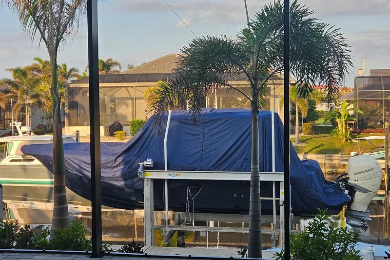 Slide: The Image of 2021 Scout 330 LXF boat covered, docked near palm trees in a residential area. - 17