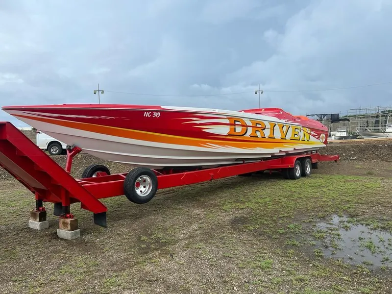 The Image of 2002 Cigarette ROUGH RIDER boat on red trailer, vibrant "DRIVEN" graphics, parked outdoors. - 1