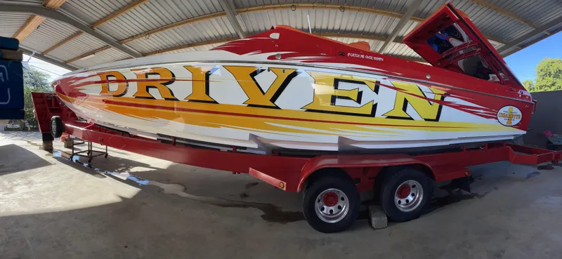 Slide: The Image of 2002 Cigarette ROUGH RIDER speedboat on trailer, vibrant "DRIVEN" graphics, under a metal roof. - 17