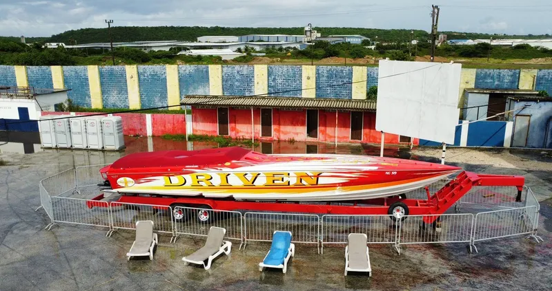 Slide: The Image of 2002 Cigarette ROUGH RIDER speedboat on trailer, vibrant "DRIVEN" design, fenced display area. - 23