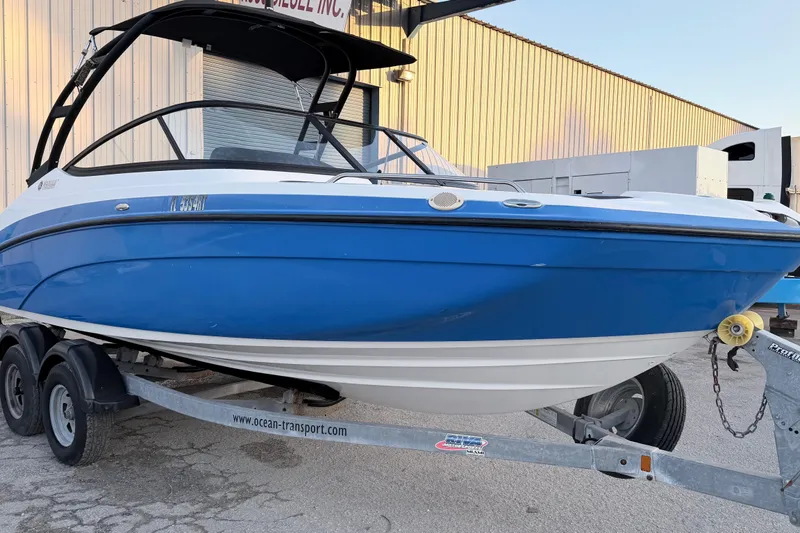 Slide: The Image of 2019 Yamaha Boats AR210 on trailer, blue and white, parked outside a building. - 2