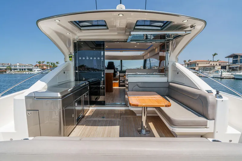 Slide: The Image of 2021 Riviera 4800 Sport Yacht interior with seating and table, docked by waterfront homes. - 27