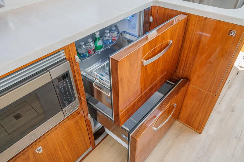 Slide: The Image of 2021 Riviera 4800 Sport Yacht kitchen with wooden cabinetry and open fridge drawers. - 38